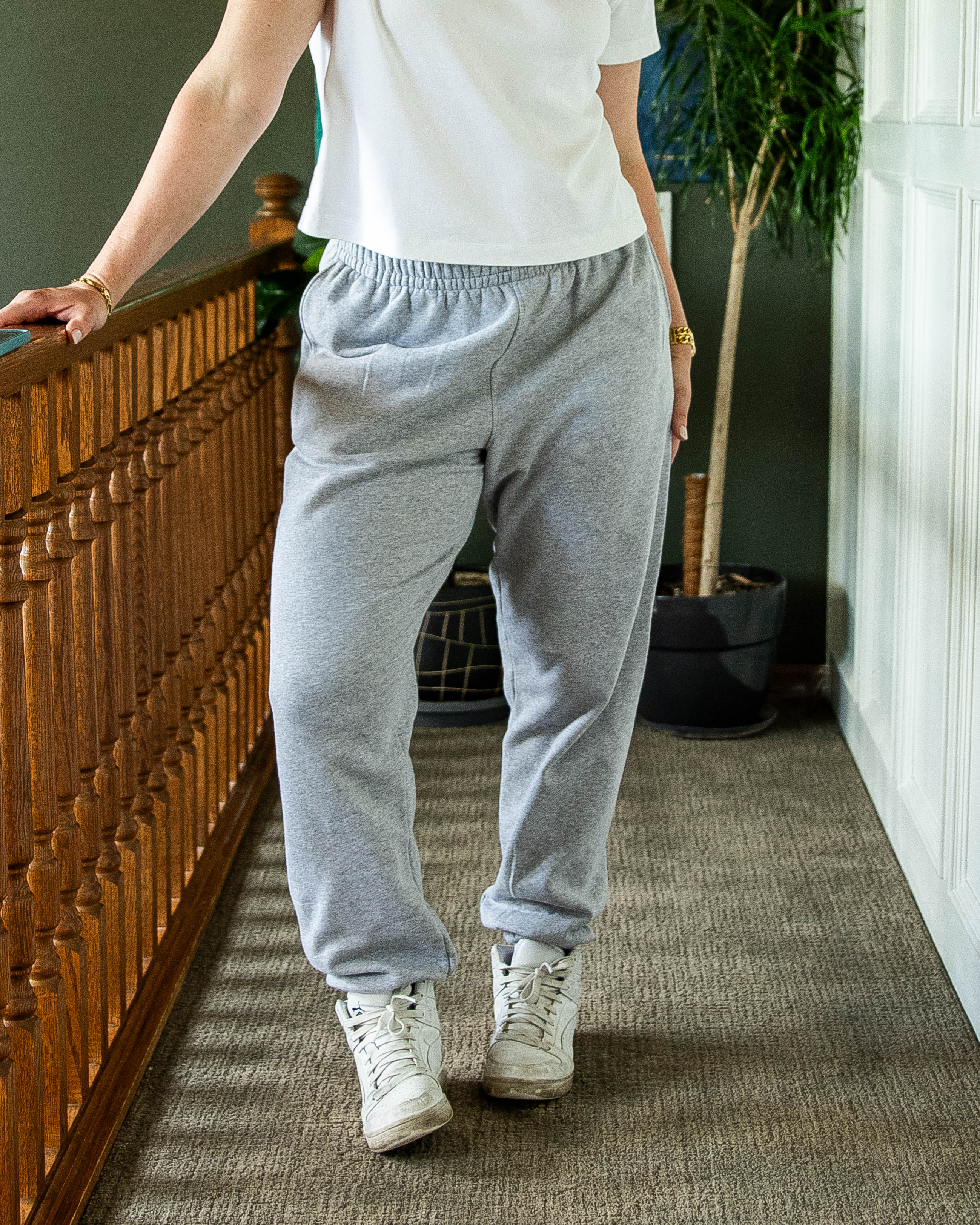 Person wearing gray sweatpants and white sneakers in a room with a wooden cabinet and plant.