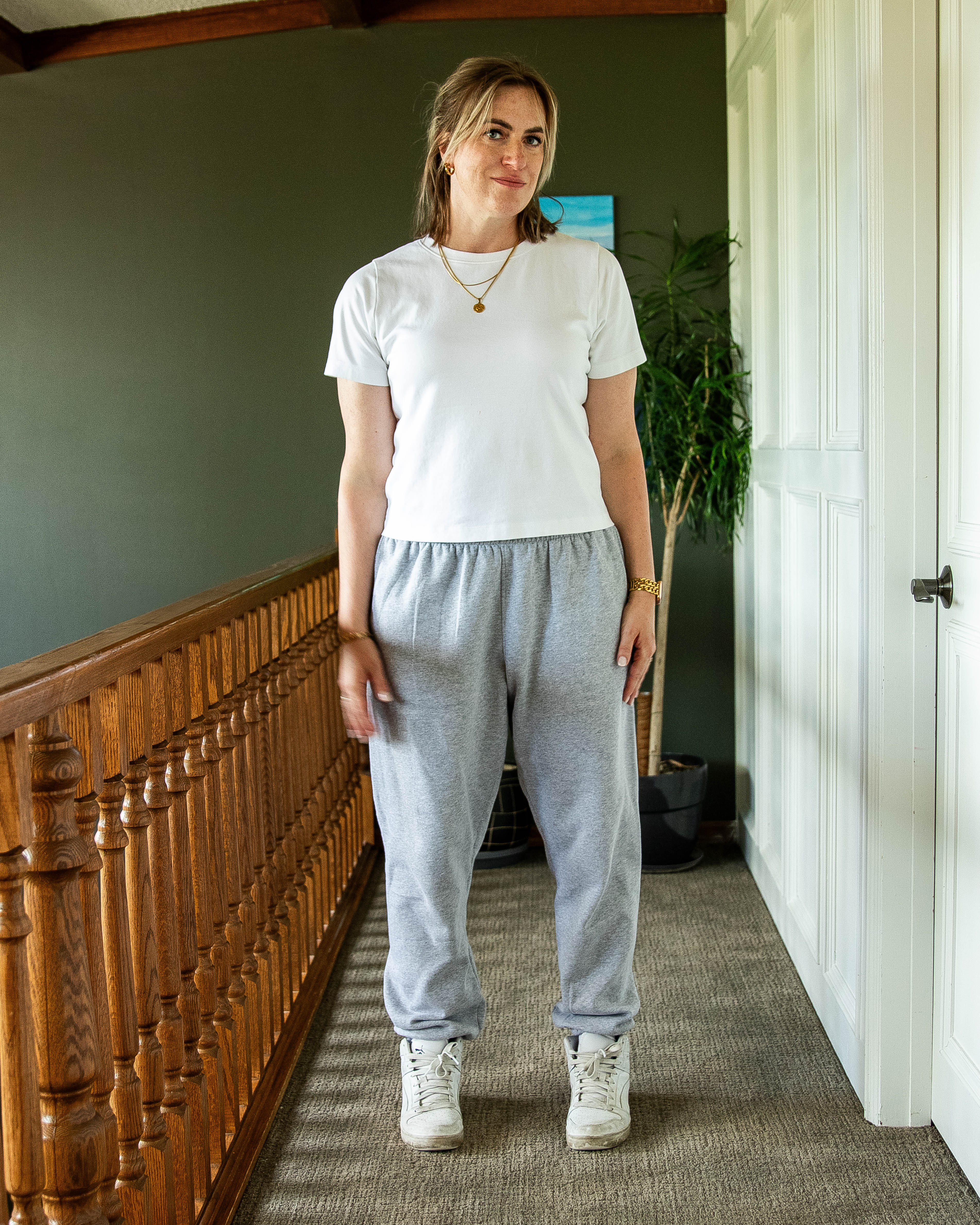 Woman wearing a white t-shirt and gray sweatpants standing in a home interior.